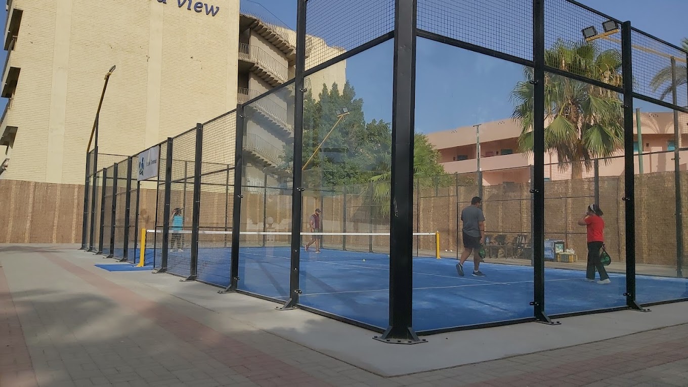 Court de padel extérieur avec parois vitrées et joueurs en action.