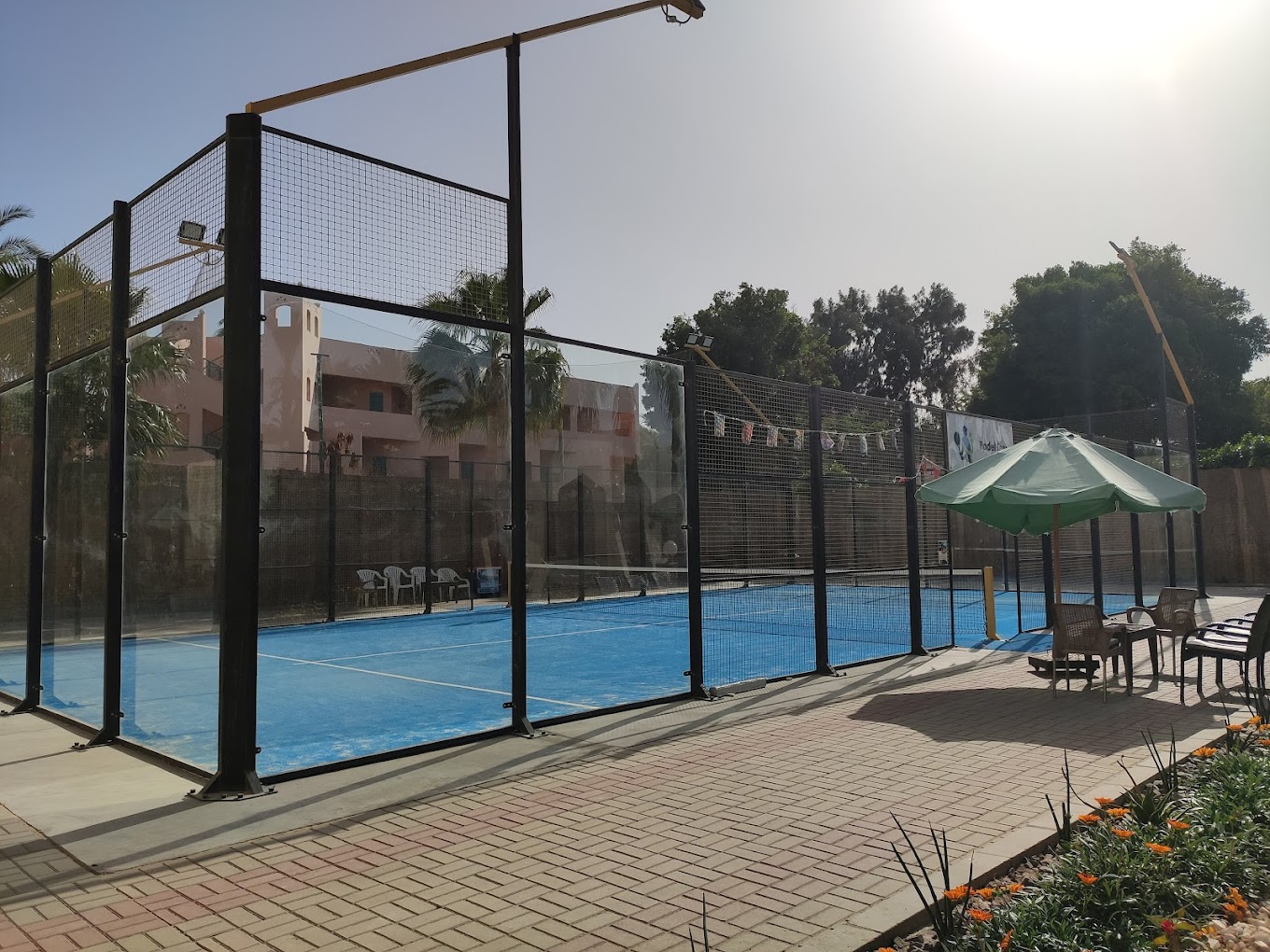 Court de padel extérieur à côté d'un coin salon avec parasol.