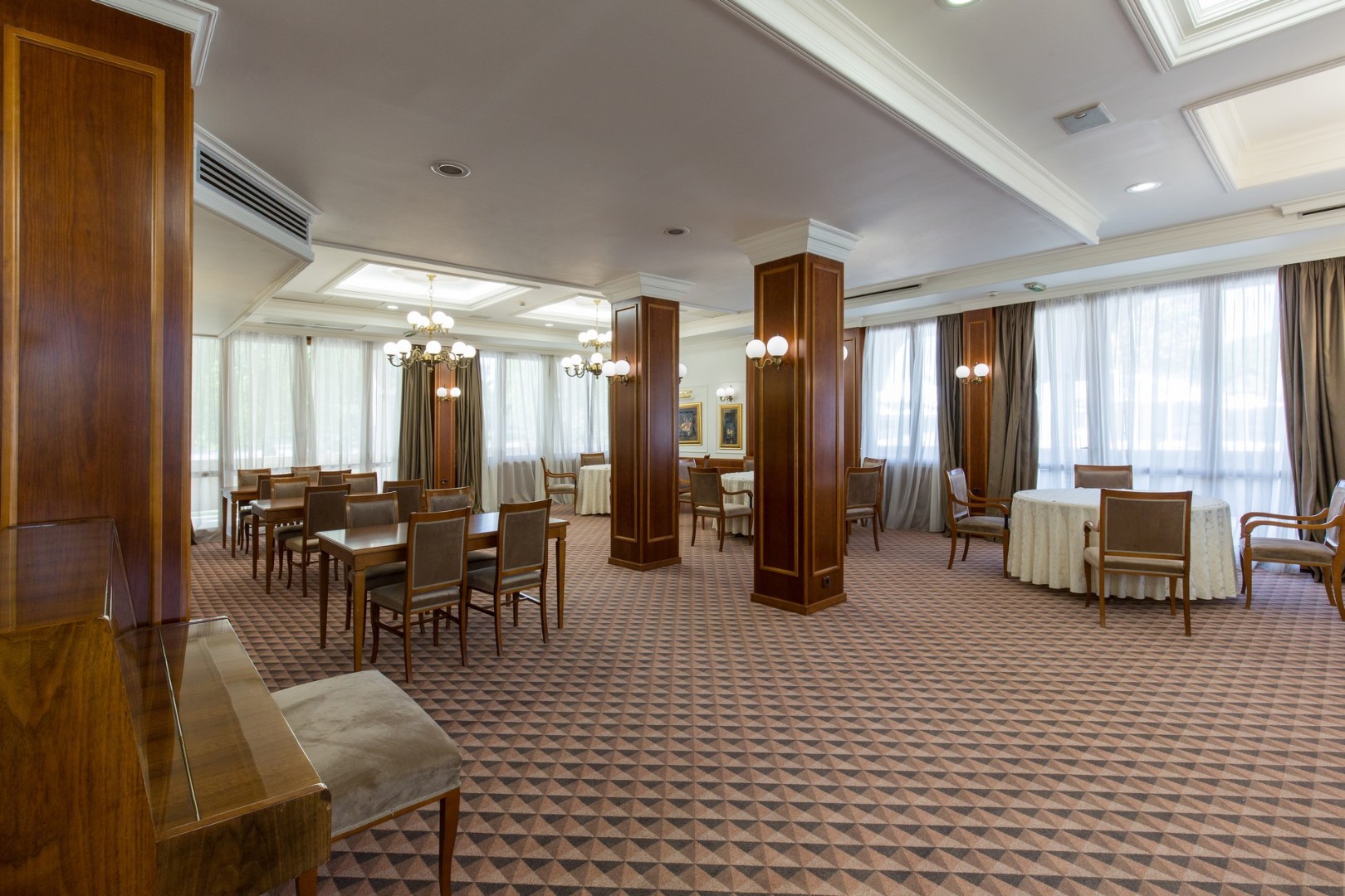 Großer Speise- oder Loungebereich mit Tischen, Stühlen, großen Fenstern und Kronleuchtern.