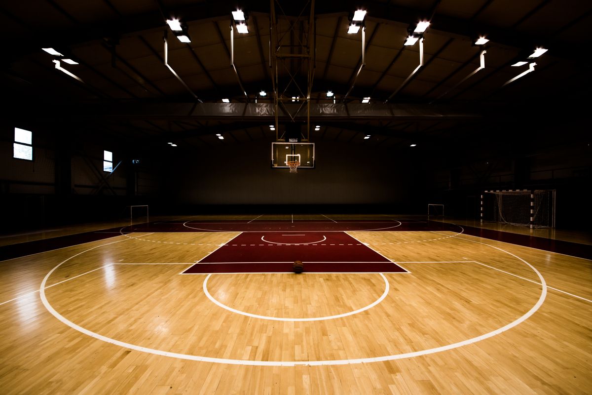 Dunkel beleuchteter Indoor-Basketballplatz mit Korb und markiertem Parkettboden.