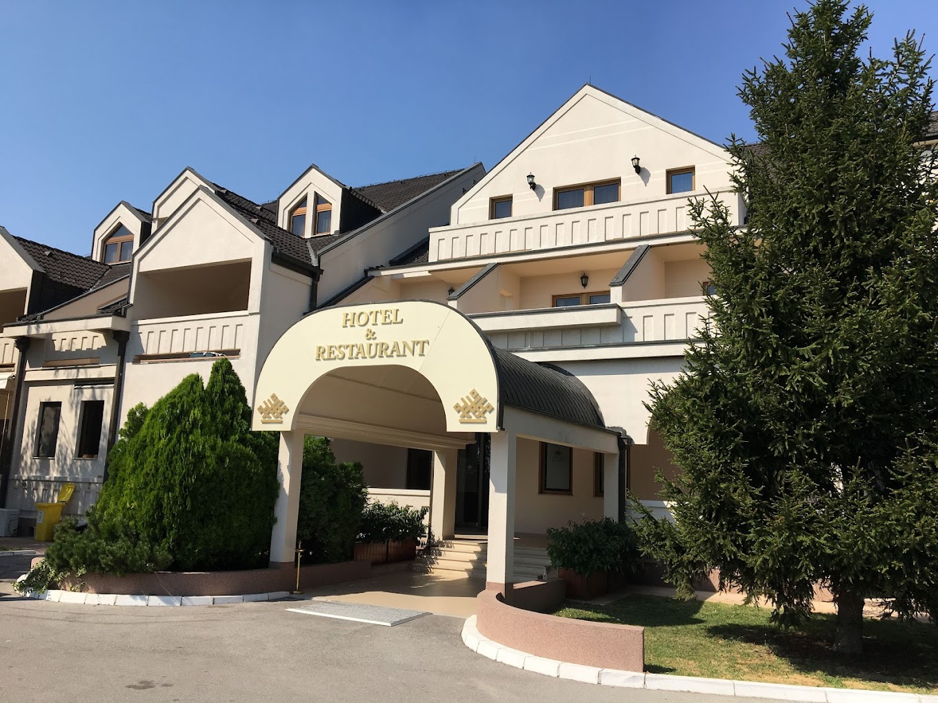 Außenansicht des Hotel- und Restaurant-Eingangs mit überdachter Zufahrt und gepflegter Begrünung.