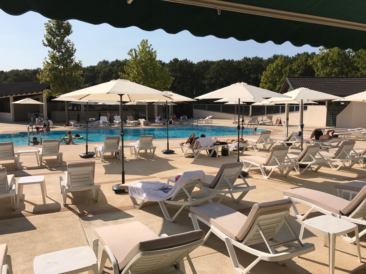 Außenpoolbereich mit Sonnenliegen, Sonnenschirmen und entspannenden Gästen.