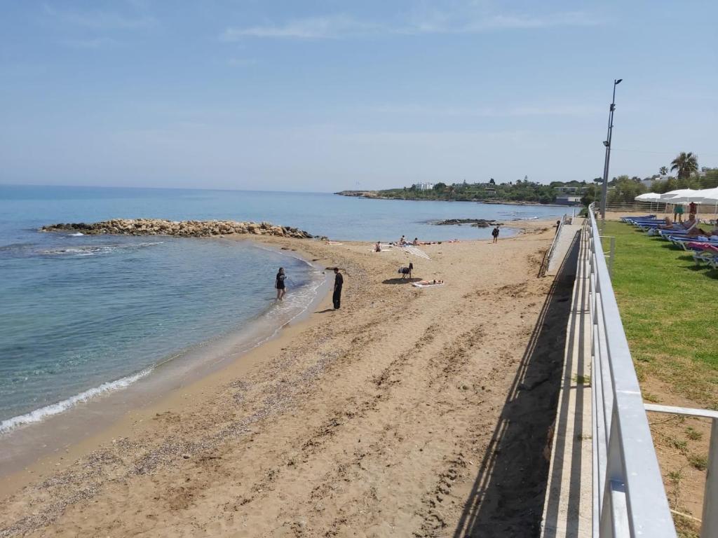 Sandy beach with calm sea, small breakwater, and seaside promenade with sun loungers.