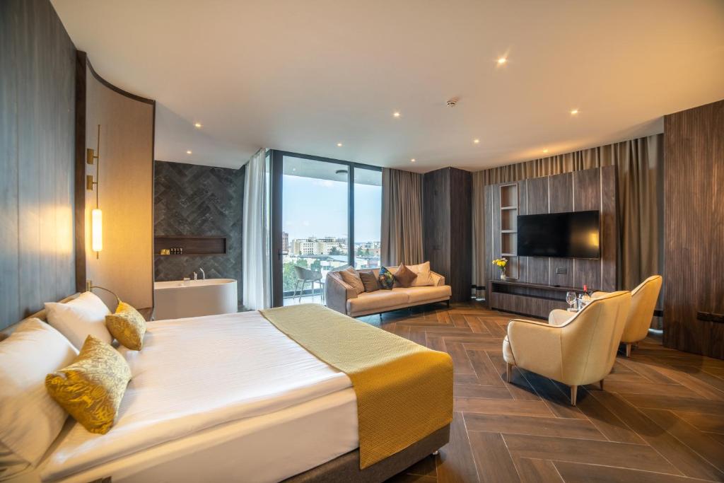 Stylish suite with double bed, sofa, large TV wall, and a bathtub area, with city views from the balcony.