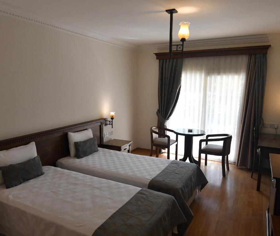 Twin-bed hotel room with small round table and balcony door with curtains.