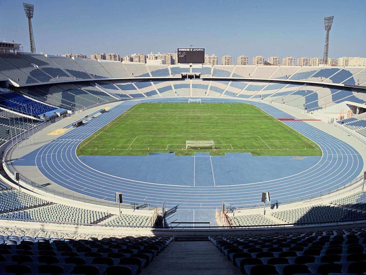Leeres Leichtathletikstadion mit blauer Laufbahn rund um ein Fußballfeld.