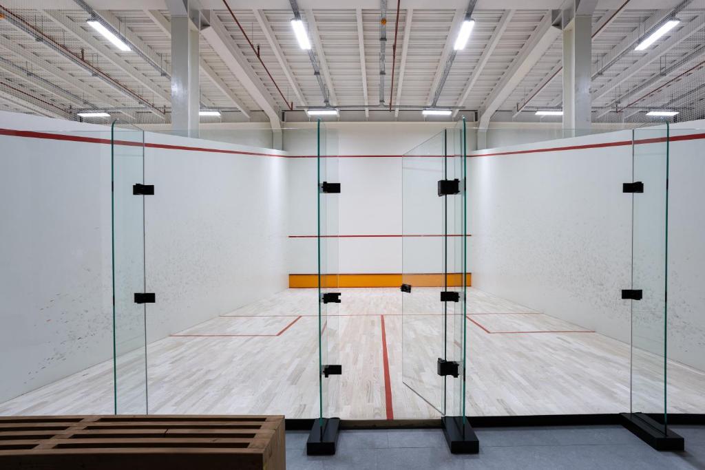 Squash-Court mit Glasrückwand, Holzboden und Sitzbank.