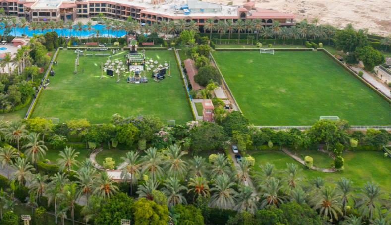 Aerial view of resort grounds with outdoor pools and two rectangular grass fields by the hotel.
