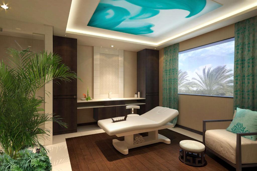 Spa treatment room with massage table and large window overlooking palm trees.