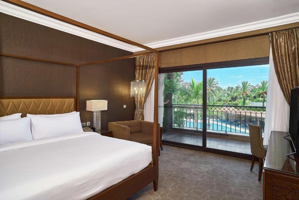 Guest room with double bed and balcony doors overlooking palm trees and the pool area.