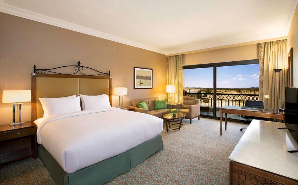Guest room with a king bed, sofa seating, and balcony doors overlooking the landscape.