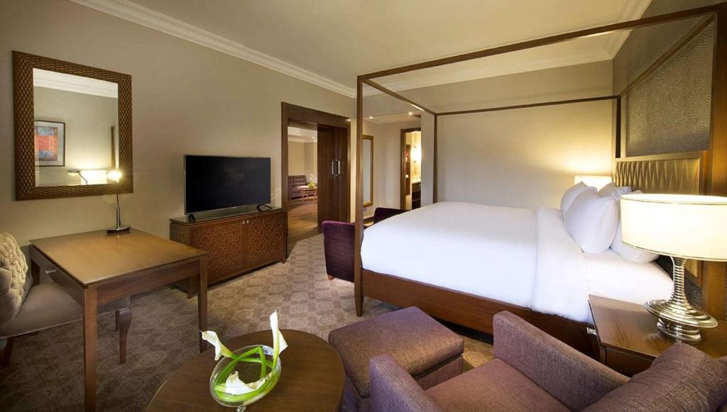 Spacious guest room with a king bed, seating area, TV, and doorway to the bathroom area.