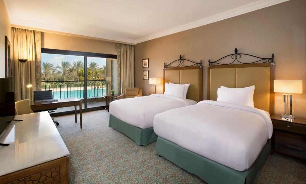 Twin guest room with two beds and a balcony overlooking palm trees and the pool area.