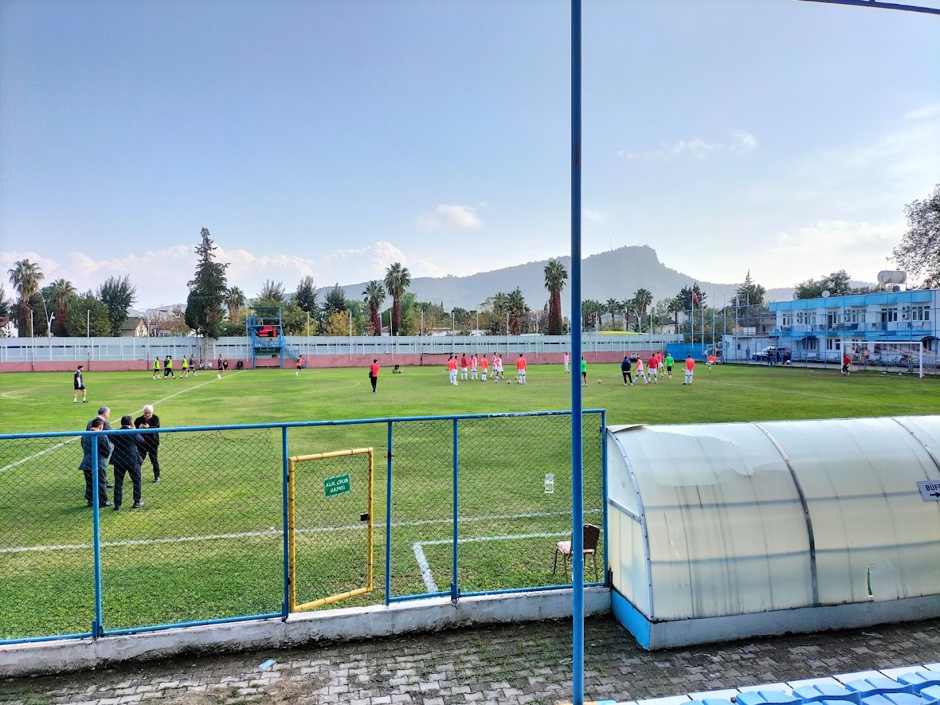 Exercices de stage de football sur un terrain de stade en herbe, avec abri de touche et montagnes en arrière-plan.