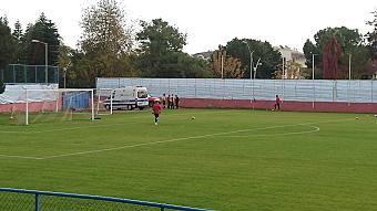 Goal area on a grass pitch during football training, with cones, balls and an ambulance behind the net.