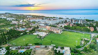 Sunset aerial of resort grounds and a football pitch overlooking the sea.