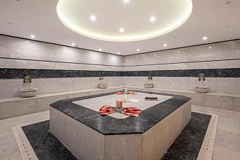 Turkish bath hammam with marble heating platform and wall fountains under circular ceiling light.