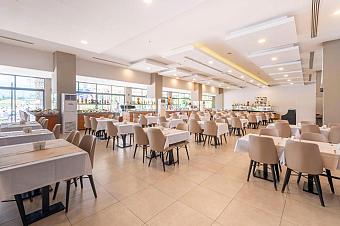 Spacious hotel restaurant with rows of tables, buffet counters, and ceiling lighting.