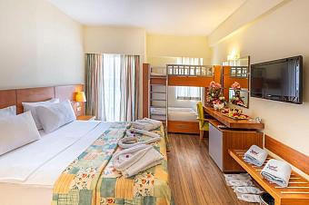 Hotel family room with double bed, bunk beds, desk, TV, and balcony curtains.