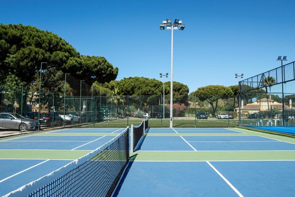 Court de tennis extérieur avec filet, éclairage et clôture périphérique.