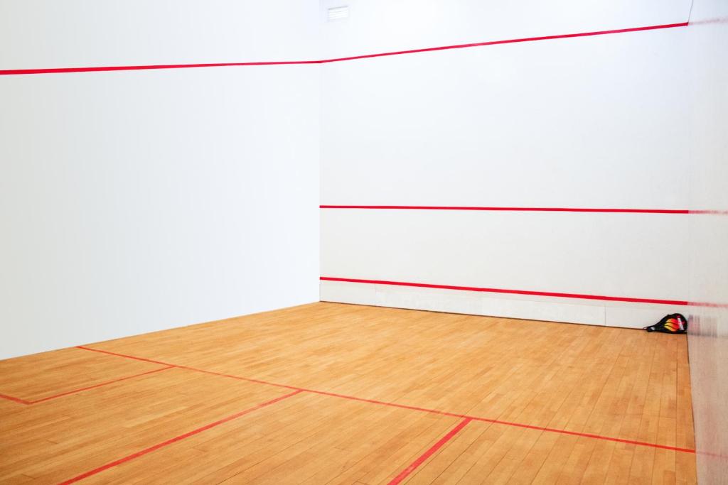 Court de squash intérieur avec parquet et lignes de délimitation rouges.