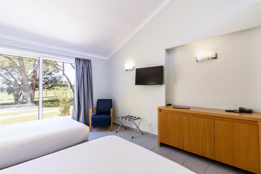 Chambre twin avec TV, rangement et grande fenêtre donnant sur le domaine.