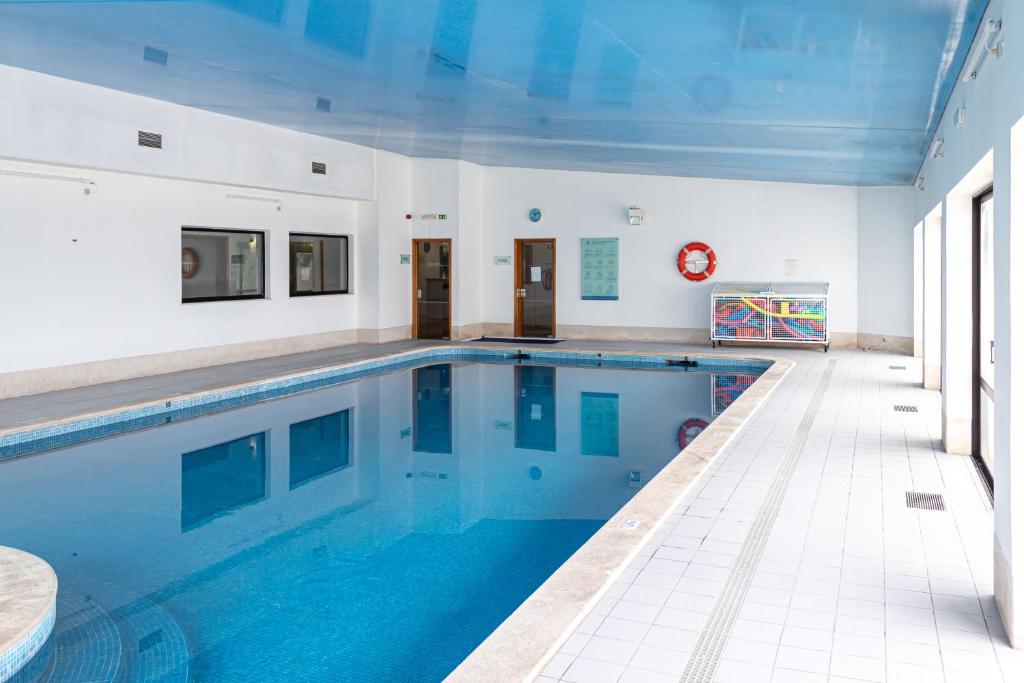 Piscine couverte avec plage carrelée et bouée au mur.
