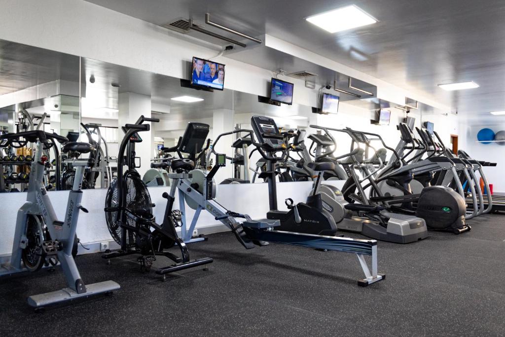 Salle de fitness avec appareils cardio, rameur et mur miroir.