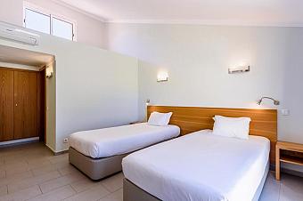 Zweibettzimmer mit zwei Einzelbetten, Nachttisch und Wandleuchten.