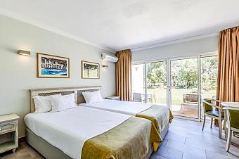 Zweibettzimmer mit Schiebetüren zur Terrasse/Garten, Klimaanlage und kleiner Sitzecke.