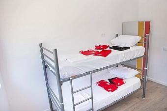 Helles Zimmer mit Etagenbett, weißer Bettwäsche und gefalteter Trainingslager-Sportkleidung.