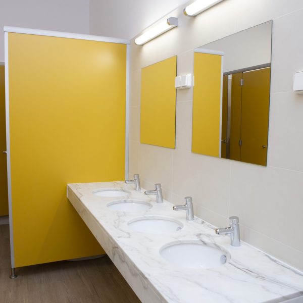 Salle de bains commune moderne avec quatre lavabos, miroirs et cloisons jaunes.
