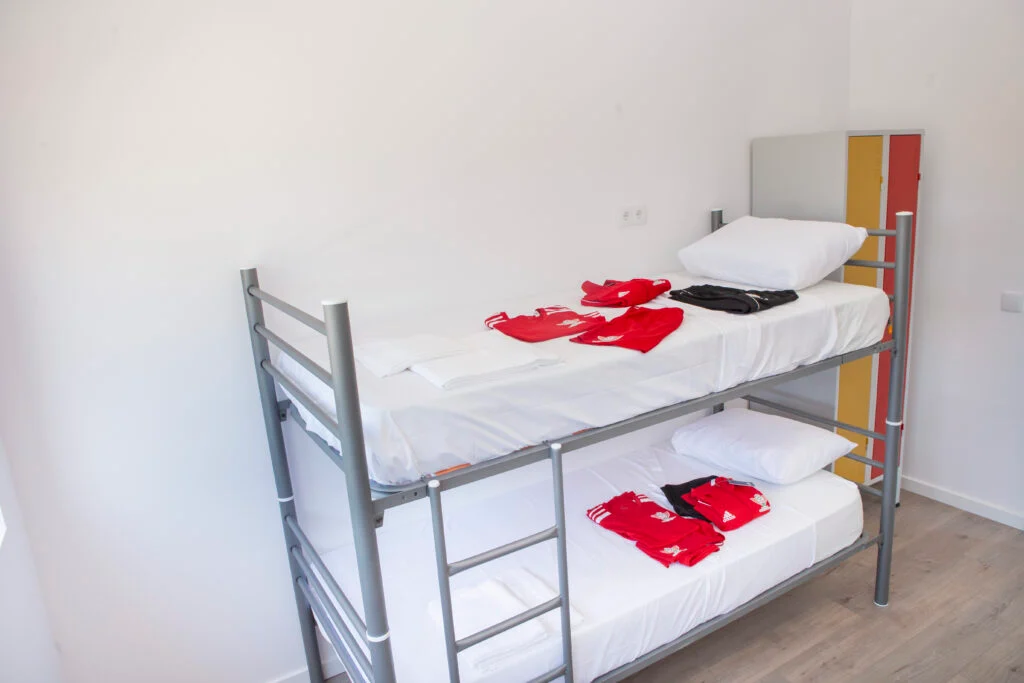 Chambre lumineuse avec lits superposés, literie blanche et vêtements de sport de camp d'entraînement pliés.