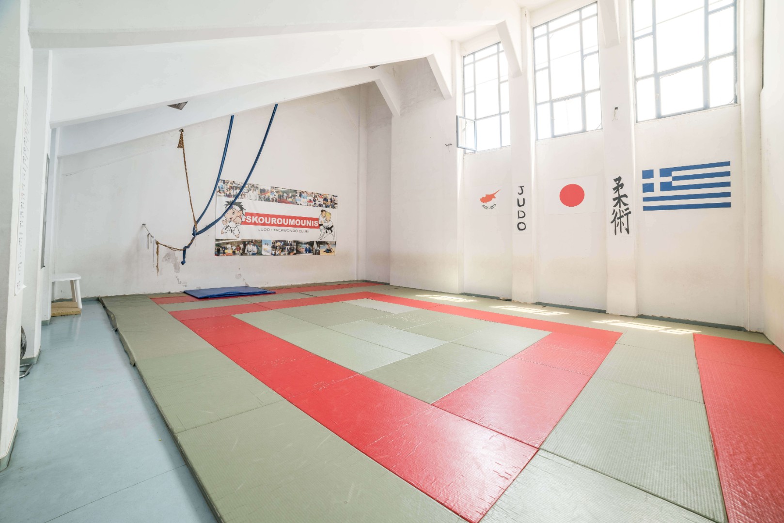 Judo-Dojo mit Tatami-Matten, Wandgrafiken und hohen Fenstern.