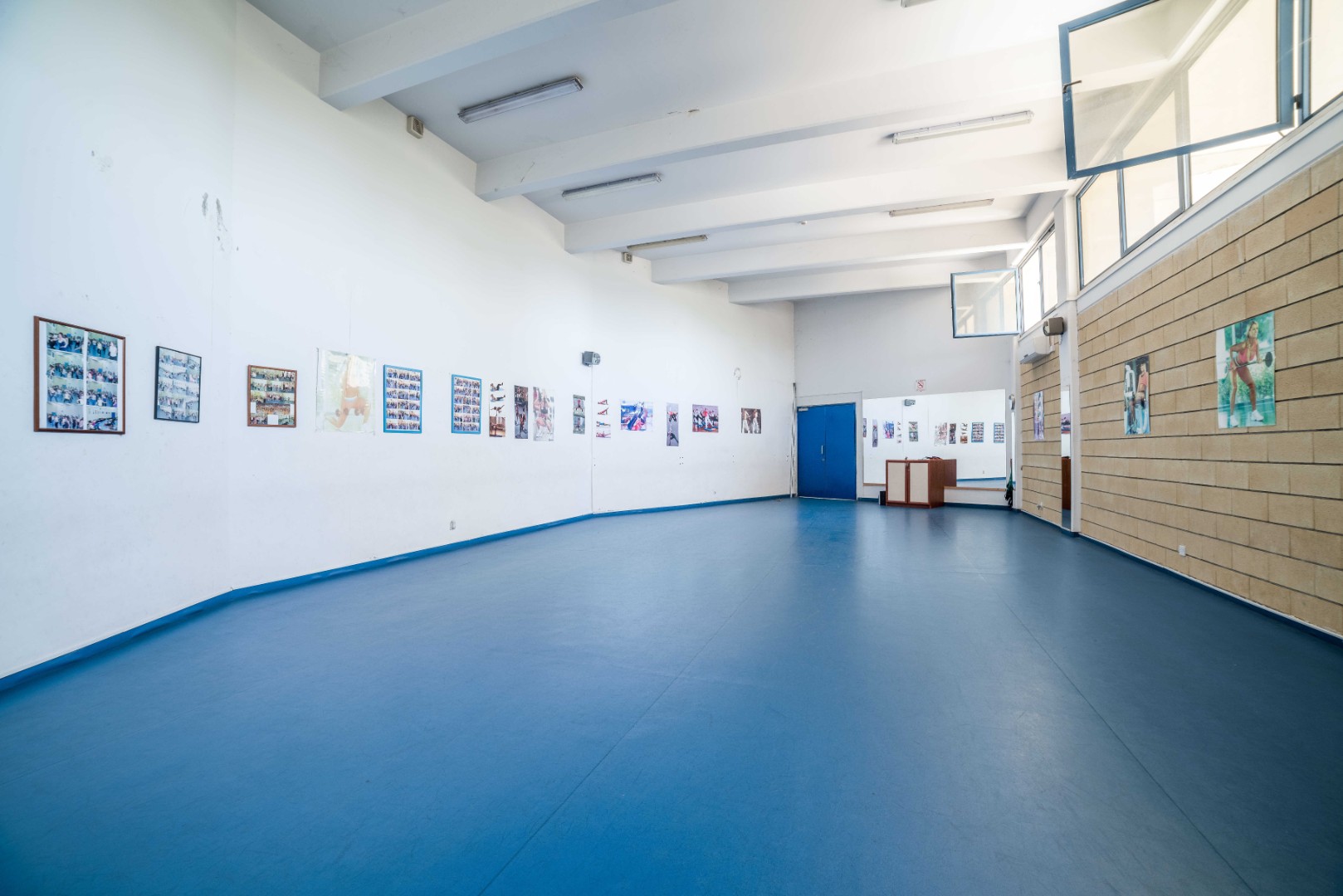 Offenes Trainingsstudio mit blauem Boden, Spiegeln und Sportfotos an den Wänden.