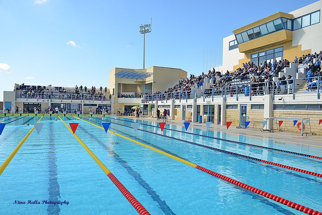 Outdoor-Schwimmanlage mit Tribünenplätzen, Zuschauern und Wettkampfbahnen.