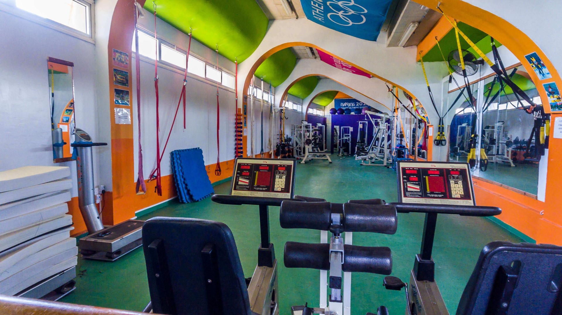 Farbenfrohes Fitnessstudio mit Cardio- und Kraftgeräten, Spiegeln und Schlingentrainern.