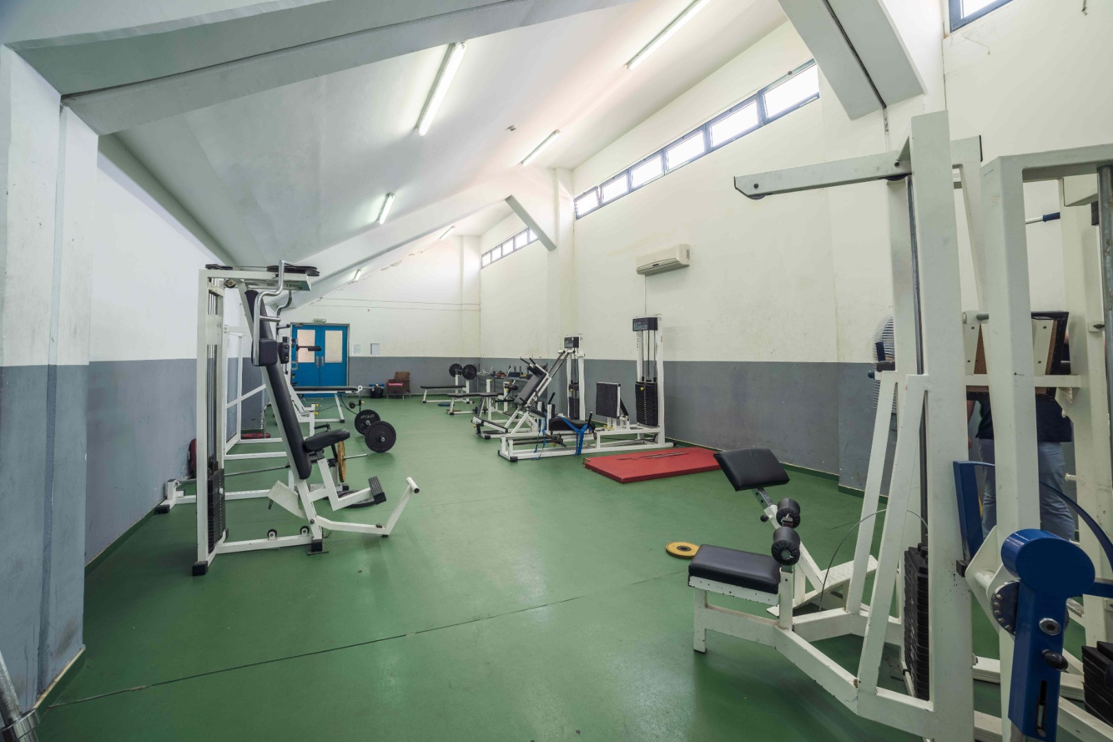 Fitnessraum mit Kraftgeräten, Bänken und Gewichten.