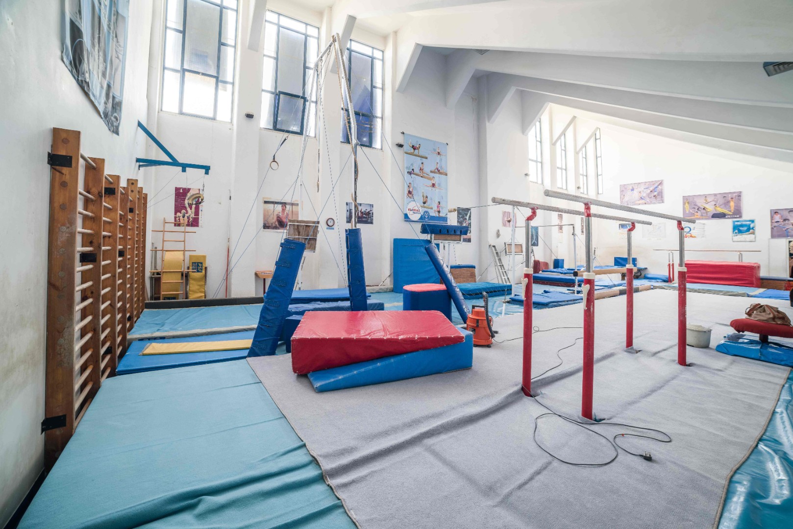 Turnhalle mit Stufenbarren, Ringen, Sprossenwand und Sicherheitsmatten.