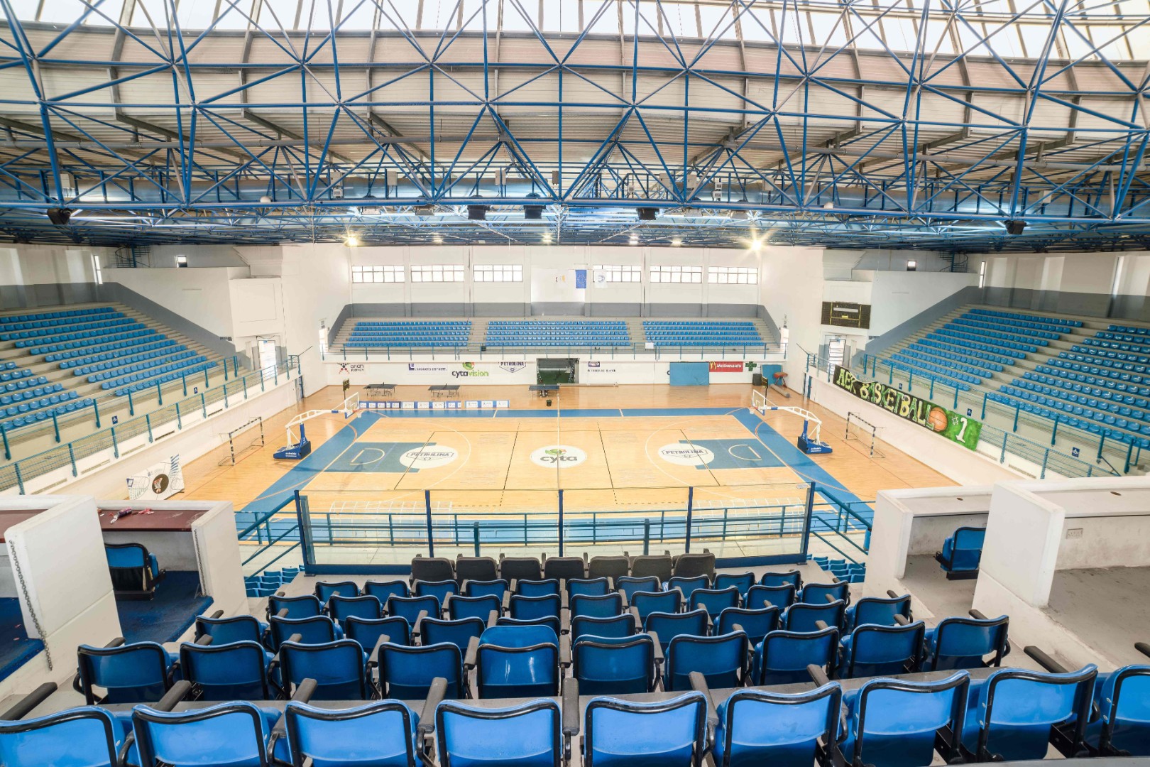 Indoor-Sportarena mit Spielfeldmarkierungen, Körben und blauen Sitzreihen.