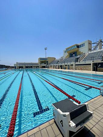 Empty outdoor lap pool with starting block, grandstands and clear blue sky.
