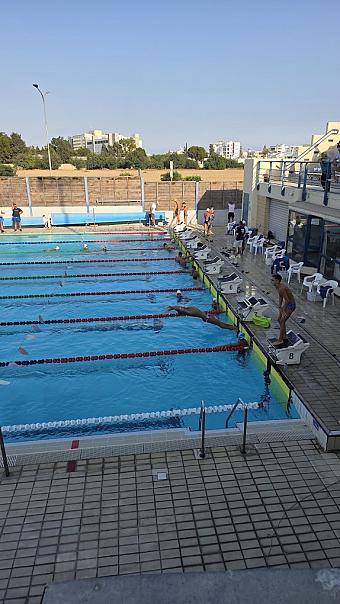 Side view of swimmers diving from starting blocks into an outdoor lap pool.
