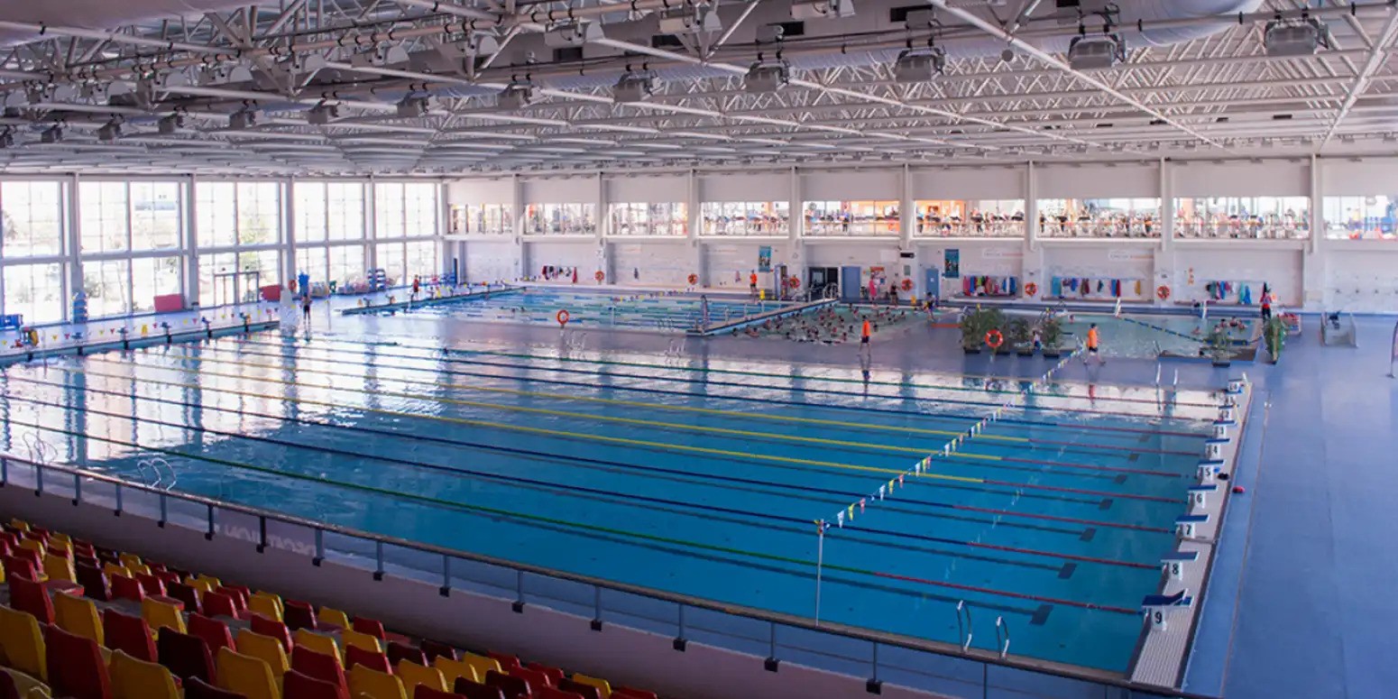 Indoor pool with several lap lanes and people swimming and standing in the water.