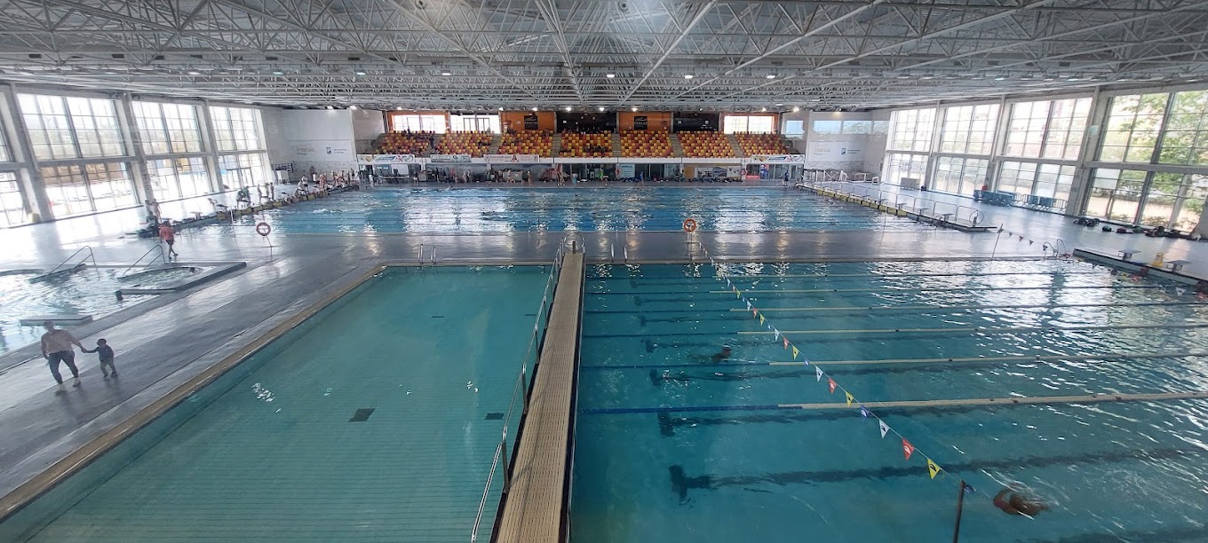 Wide view of an indoor pool complex with lap lanes, a second pool, and a few swimmers.