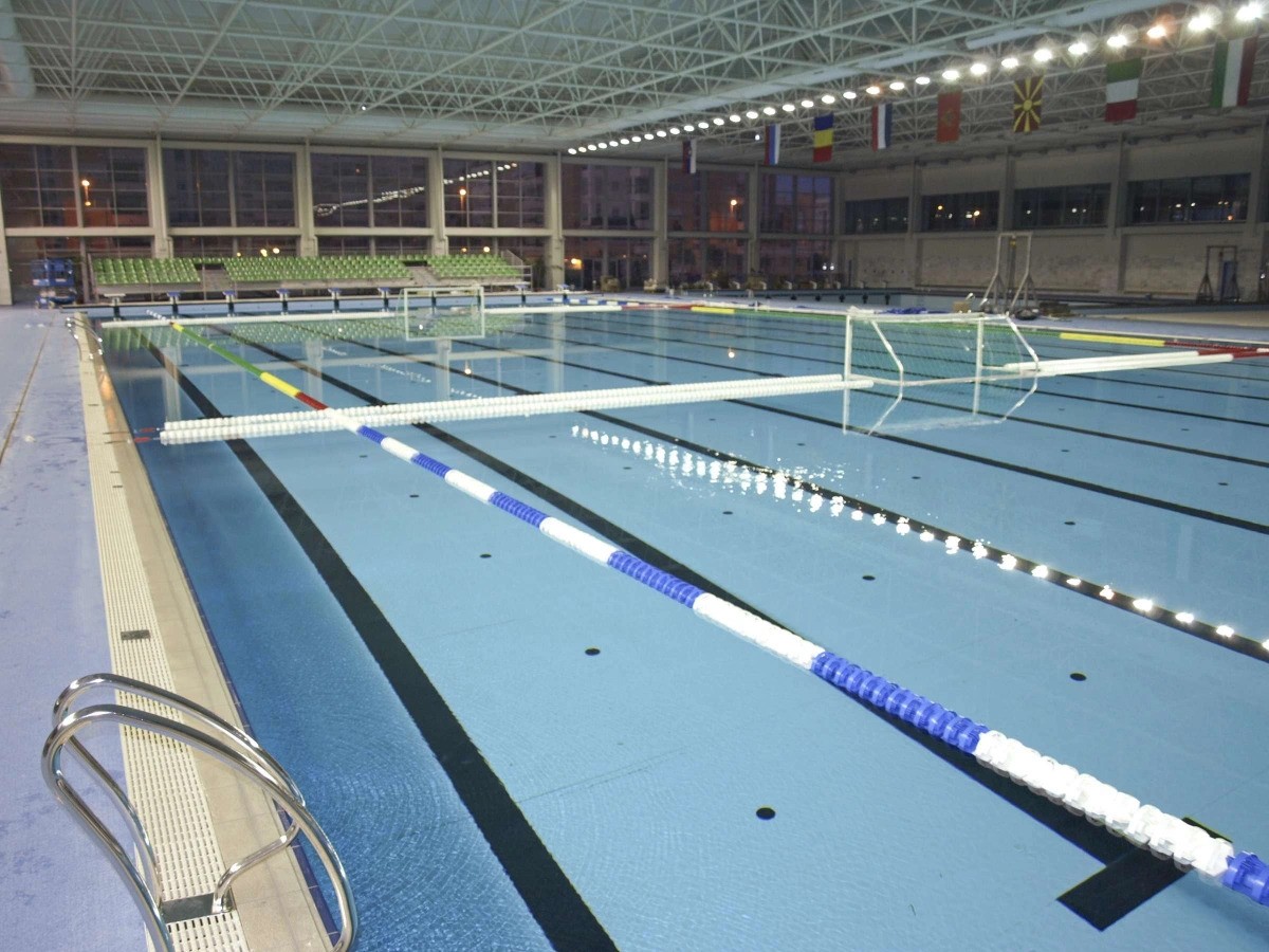 Indoor pool set up for water polo with goals, lane ropes, and deck lighting.