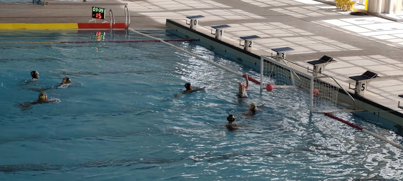 Water polo action near the goal with players defending and attacking.