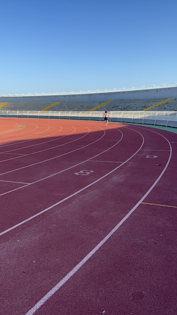 Curved athletics lanes with a person running and empty stadium seating in the background.