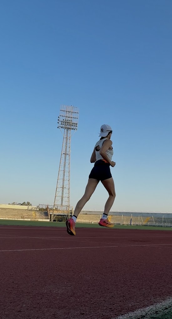 A person running on the athletics track beside a floodlight tower in the stadium.