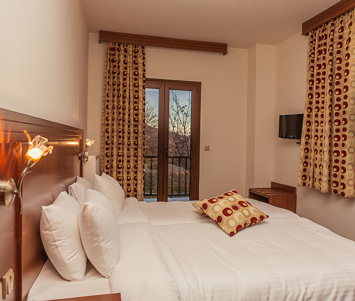Twin room with balcony door, patterned curtains and wall-mounted TV.