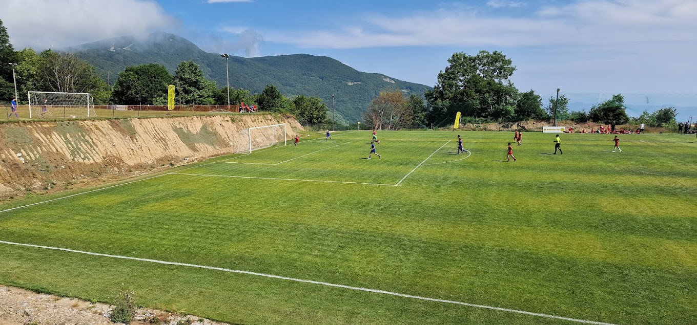 Football pitch with players in action and mountain views in the background.